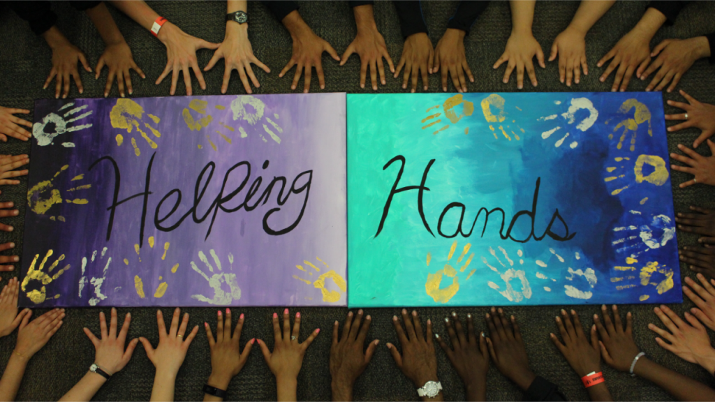 Student hands surround a poster that reads Helping Hands